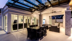 A modern interior with a glass-enclosed dining area, a stone accent wall, and a cozy seating area with a flat-screen TV. - Orchid Paradise Homes OPV401 (Hua Hin)