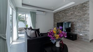 A modern living room with a black sofa, a flat-screen TV, and a stone wall. - Orchid Paradise Homes OPV301 (Hua Hin)
