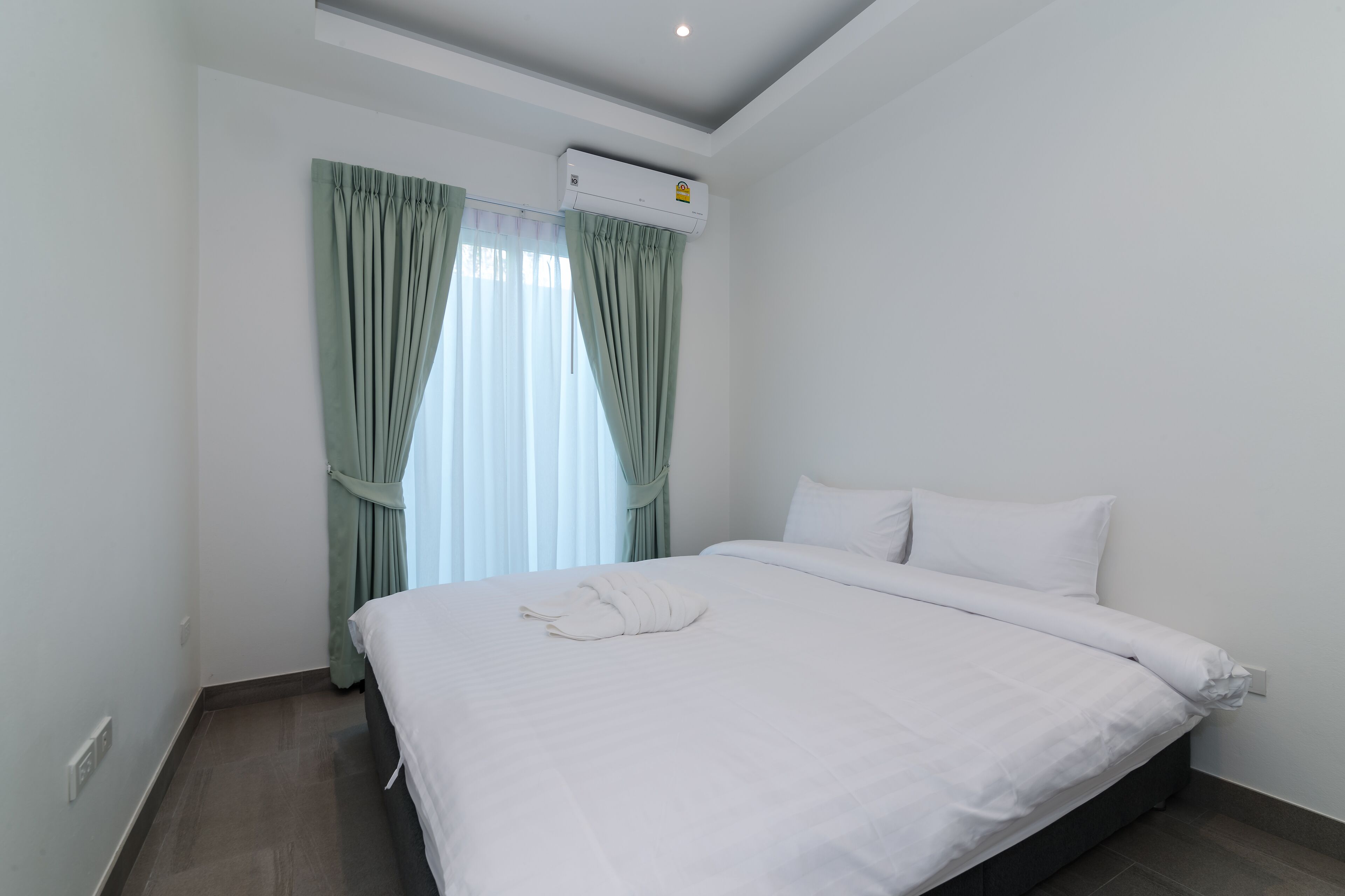 A hotel room with a large bed, a window with curtains, an air conditioning unit, and a wall socket.