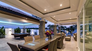 A modern outdoor living area with a pool table, comfortable seating, and a glass-enclosed space. - Orchid Paradise Homes OPV301 (Hua Hin)