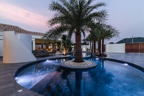 Een modern buitenzwembadgedeelte met een palmboom in het midden, omringd door een stenen terras en een loungehoek met zitplaatsen.