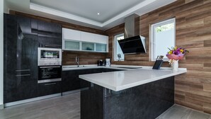 A modern kitchen with dark cabinetry, a central island, and a built-in oven. - Orchid Paradise Homes OPV301 (Hua Hin)