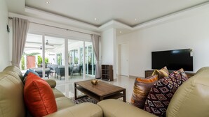 A modern living room with a sofa, a coffee table, and a flat-screen TV. - Orchid Paradise Homes OPV404 (Hua Hin)