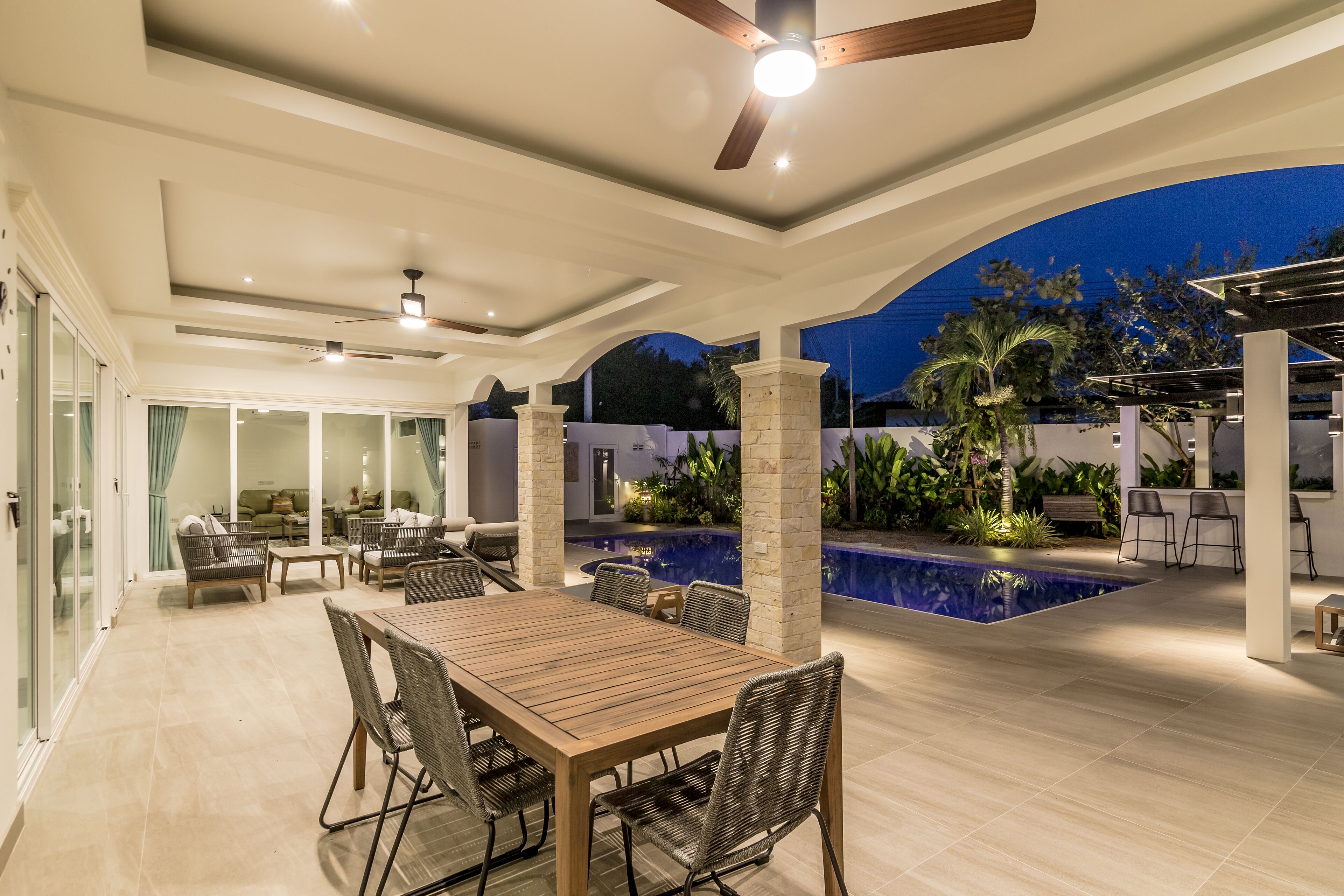 Un patio exterior con mesa, sillas, ventilador de techo y piscina.