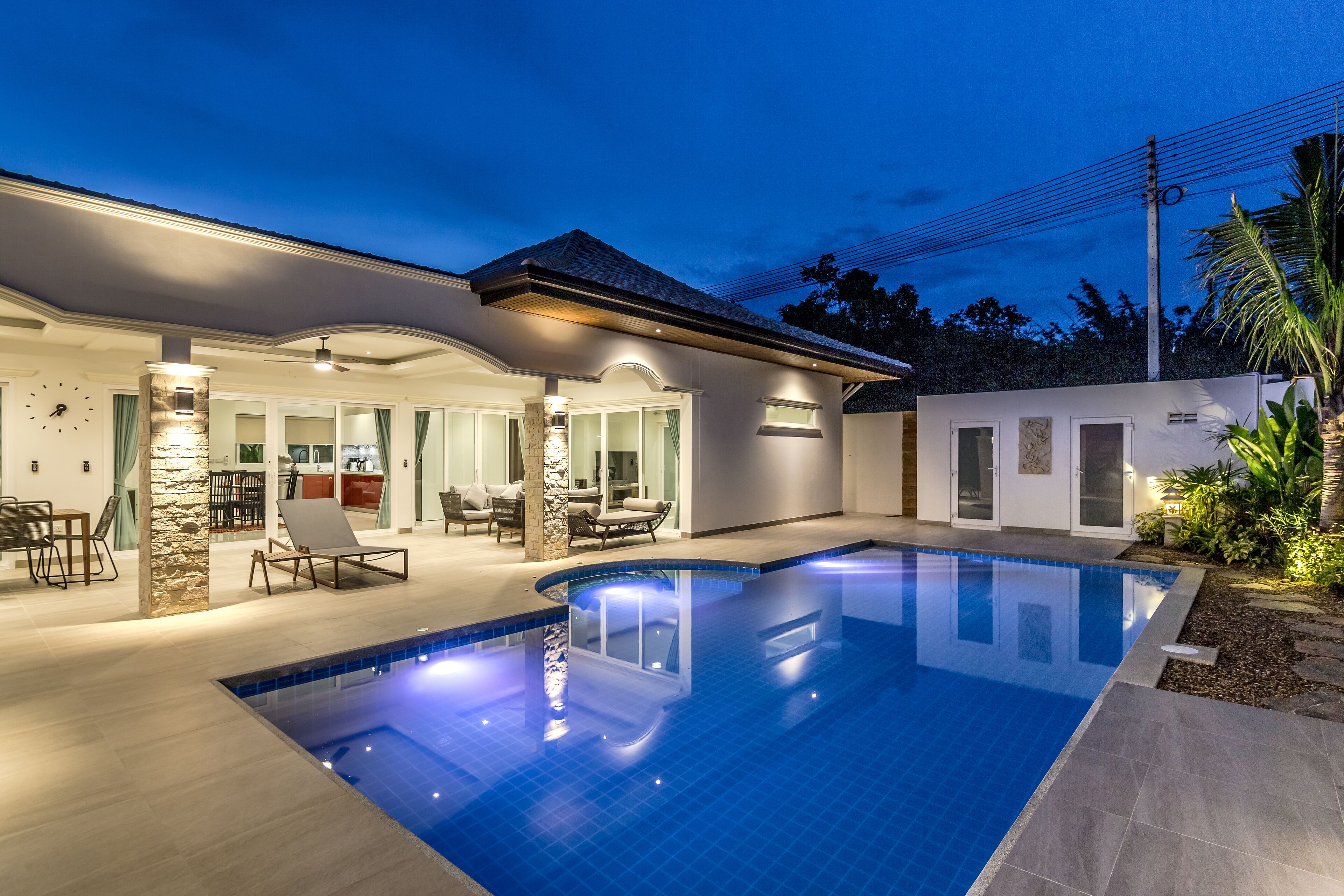 A modern house with a swimming pool, outdoor seating, and a well-lit patio area.
