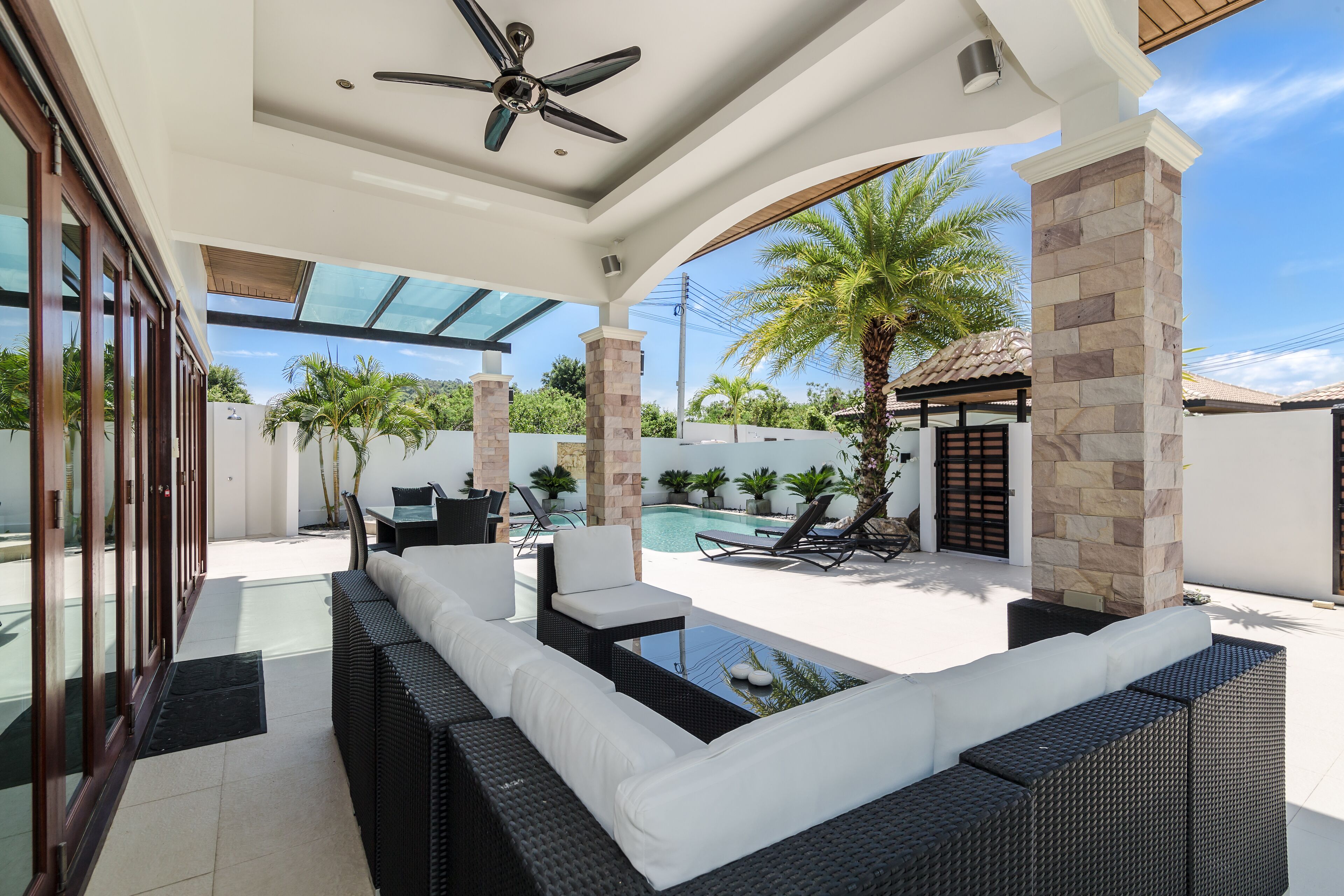 An outdoor patio with a pool, wicker furniture, and palm trees.