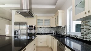 A modern kitchen with white cabinets, black countertops, stainless steel appliances, and a tiled backsplash. - Orchid Paradise Homes OPV210 (Hua Hin)