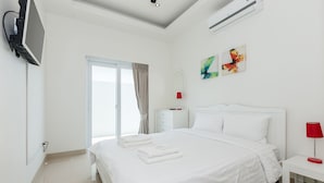A modern hotel room with a large bed, a flat-screen TV mounted on the wall, a bedside table with a red lamp, and a window with curtains. - Orchid Paradise Homes OPV219 (Hua Hin)