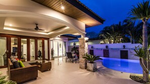 A modern outdoor living area with a pool, comfortable seating, and a well-lit ceiling. - Orchid Paradise Homes OPV209 (Hua Hin)