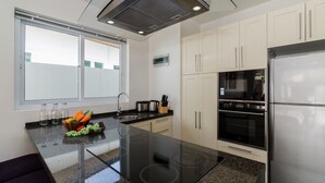 A modern kitchen with a central island, stainless steel appliances, and a large window. - Orchid Paradise Homes OPV209 (Hua Hin)