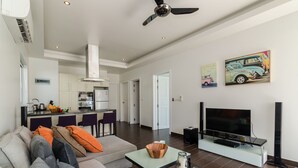 A modern living room with a sofa, coffee table, and TV. A kitchen is visible in the background. - Orchid Paradise Homes OPV209 (Hua Hin)