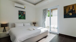 A modern bedroom with a large bed, a painting, an air conditioner, and a glass door leading to a balcony. - Orchid Paradise Homes OPV209 (Hua Hin)