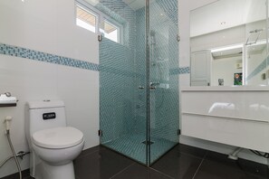 Une salle de bain moderne avec une douche à parois de verre, des toilettes blanches et un grand miroir au-dessus du lavabo.