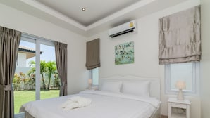 A bedroom with a large bed, a nightstand, an air conditioning unit, a window with curtains, and a view of greenery outside. - Orchid Paradise Homes OPV220 (Hua Hin)
