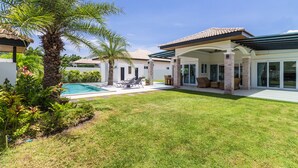 A modern house with a swimming pool, covered patio, and lush landscaping. - Orchid Paradise Homes OPV220 (Hua Hin)