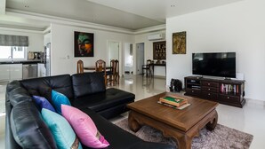 A modern living room with a black leather sofa, a wooden coffee table, and a flat-screen TV. - Orchid Paradise Homes OPV220 (Hua Hin)