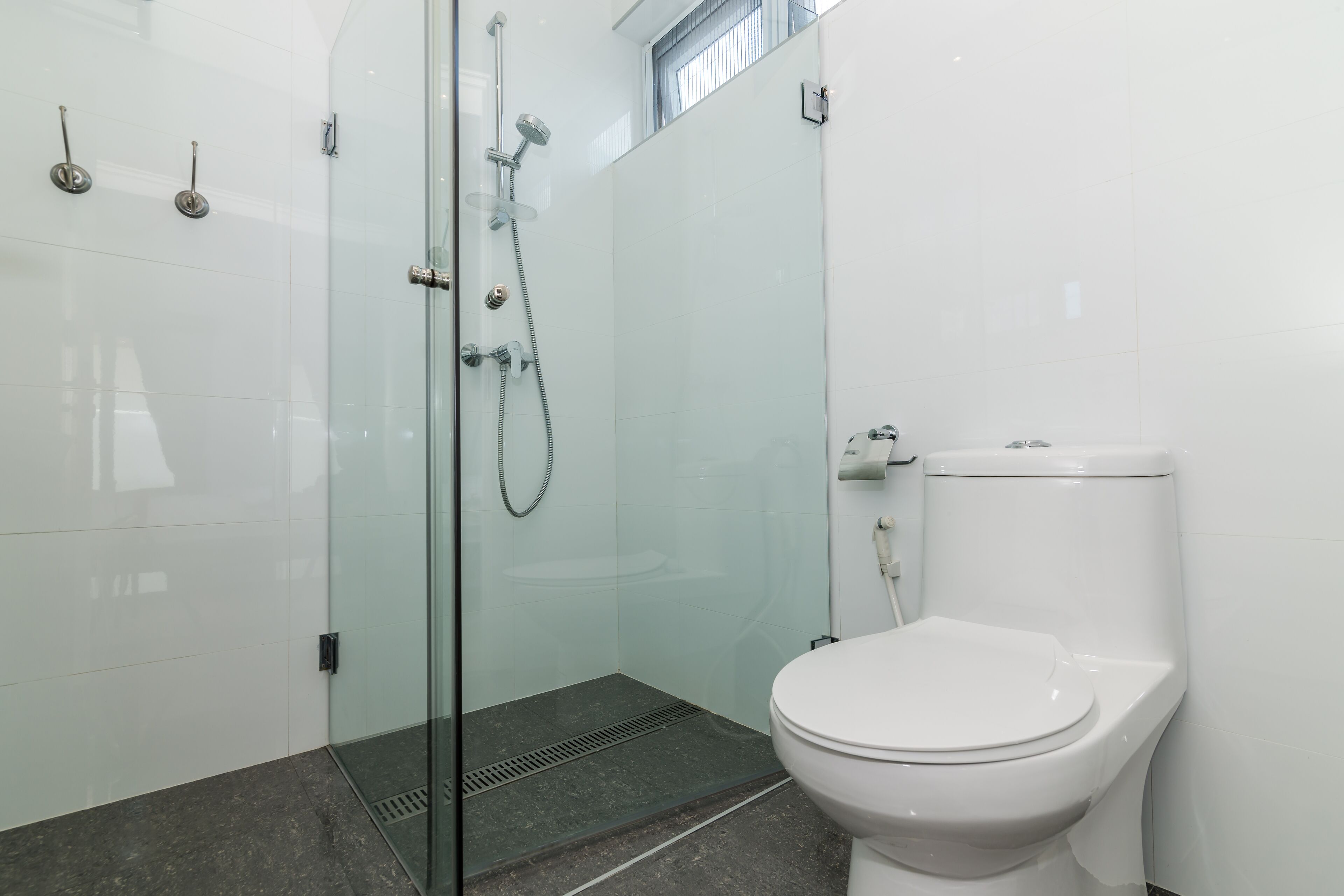 Une salle de bain moderne avec une douche à parois de verre, des toilettes blanches et un sol carrelé.