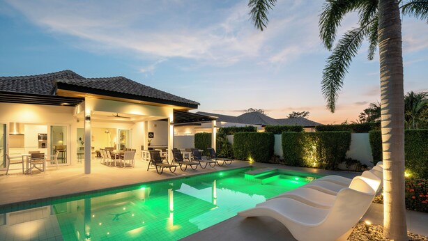 Un espace piscine extérieur moderne, doté d’un coin salon couvert, de chaises longues et d’une terrasse bien éclairée.