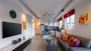 A modern living room with a flat-screen TV, a coffee table, and a sofa with colorful cushions. - Orchid Paradise Homes OPV213 (Hua Hin)