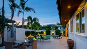 An outdoor patio with wicker furniture, a pool, and palm trees. - Orchid Paradise Homes OPV213 (Hua Hin)