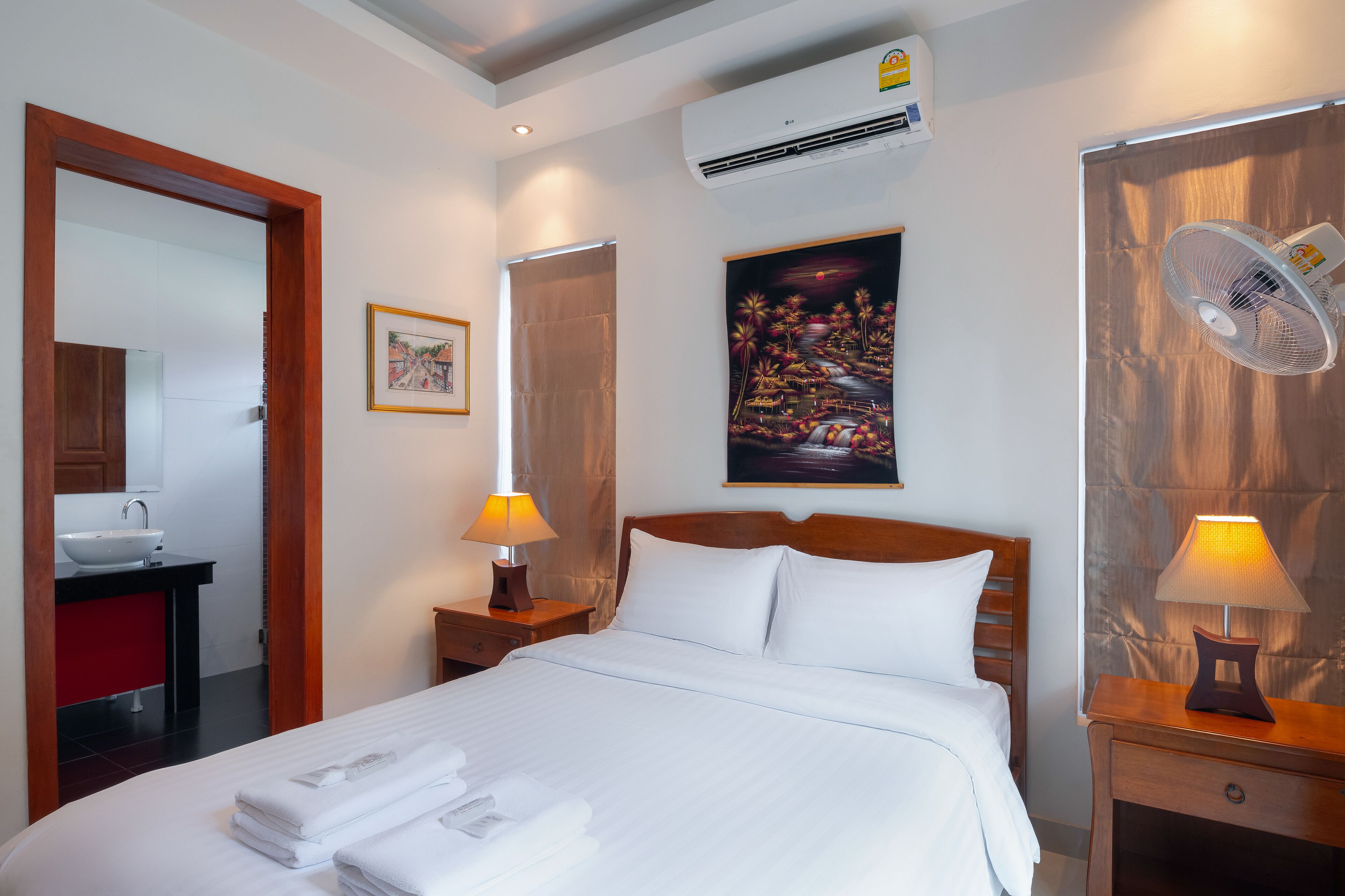 Habitación de hotel con cama, mesita de noche con lámpara, cabecero de madera, aire acondicionado, un cuadro en la pared y un espejo.