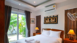 A hotel room with a large bed, two bedside tables with lamps, an air conditioning unit, a window with curtains, and a wall-mounted artwork.