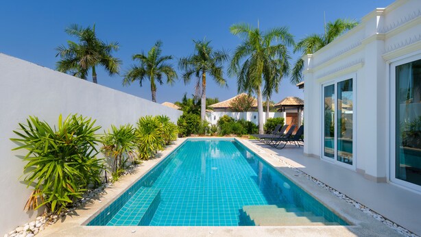 A rectangular swimming pool with clear blue tiles, surrounded by white walls and palm trees. - Orchid Paradise Homes OPV315 (Hua Hin)