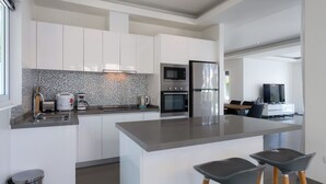 A modern kitchen with white cabinets, a large island, stainless steel appliances, and a coffee maker. - Orchid Paradise Homes OPV315 (Hua Hin)