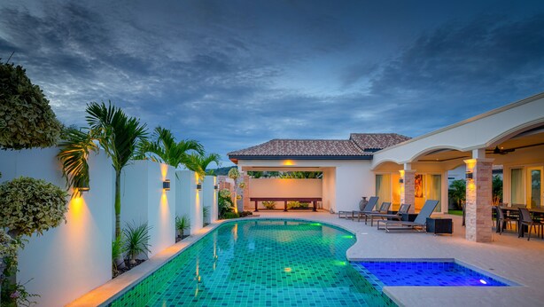 A swimming pool with a tiled deck, surrounded by a patio area with chairs and a table. - Orchid Paradise Homes OPV515 (Hua Hin)