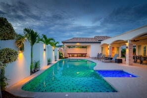 A swimming pool with a tiled deck, surrounded by a patio area with chairs and a table. - Orchid Paradise Homes OPV515 (Hua Hin)