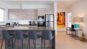 A modern kitchen with a central island, bar stools, a refrigerator, an oven, and a coffee maker. - Orchid Paradise Homes OPV515 (Hua Hin)