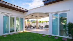 A covered outdoor patio with a dining area, sliding glass doors, and a well-maintained lawn. - Orchid Paradise Homes OPV515 (Hua Hin)