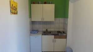 Cocina pequeña con armarios blancos, un fregadero y una estufa. Hay un cubo de basura azul y un electrodoméstico blanco pequeño en la encimera.