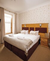 Una cama bien hecha con un plaid de diseño herringbone, una mesita de noche de madera con lámpara y una ventana con cortinas.