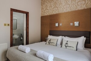 Una habitación de hotel con cabecera de madera, ropa de cama blanca y dos almohadas decorativas.