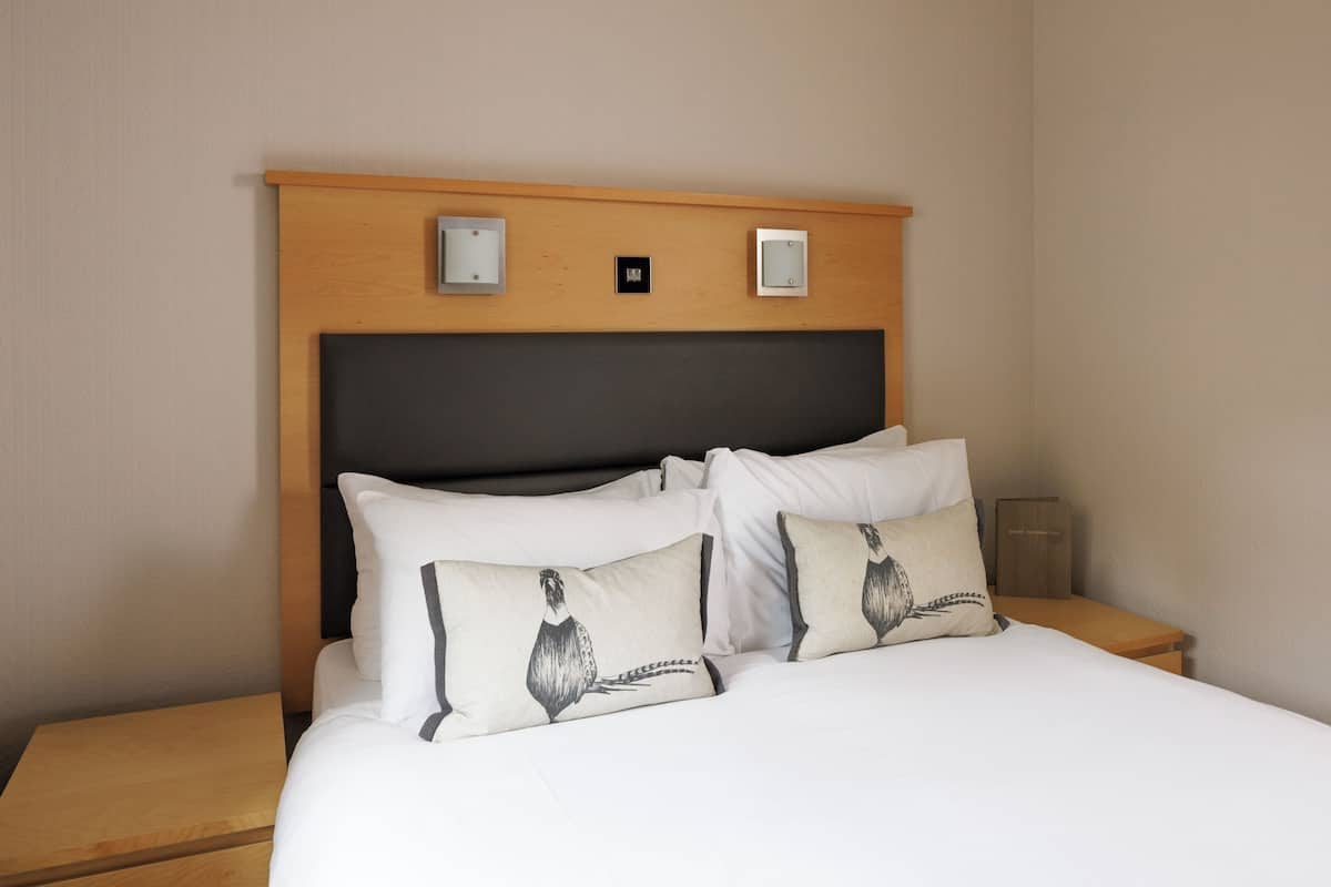 Une chambre d’hôtel avec un lit, deux tables de chevet et une tête de lit en bois dotée de deux interrupteurs pour les lampes.