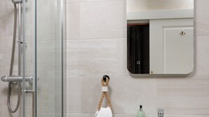 Ein Badezimmer mit Duschkabine aus Glas, einem weißen Waschbecken mit Spiegel darüber und einem Handtuch an einem Haken.