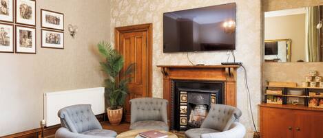 Sala de estar con dos sillones grises, una mesa de centro de madera, una chimenea, un televisor de pantalla plana, cuadros enmarcados en la pared y un espejo grande.