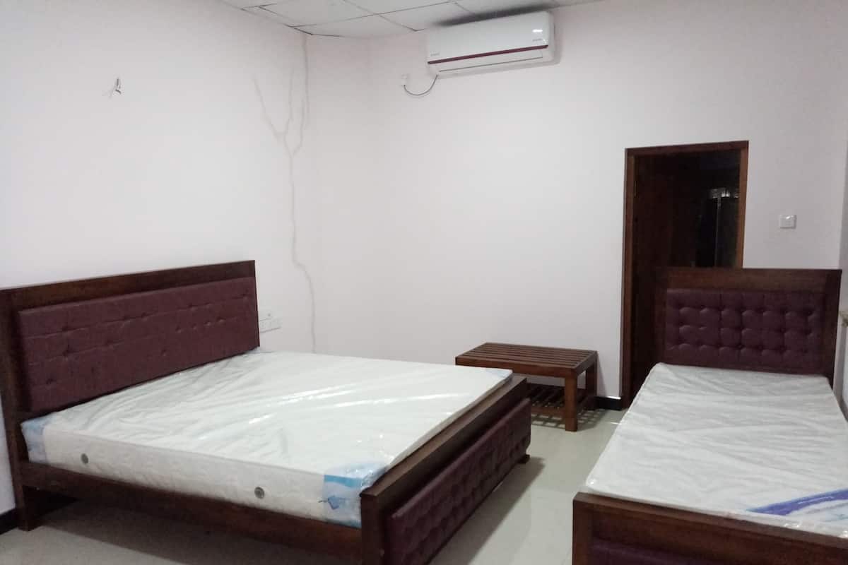 A room with two beds, a small table, and an air conditioning unit.