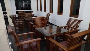 Un comedor con mobiliario de madera y una mesa con superficie de vidrio, paredes blancas y ventanas.