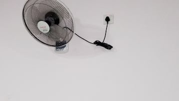 A standing fan with a power cord plugged into a wall socket.