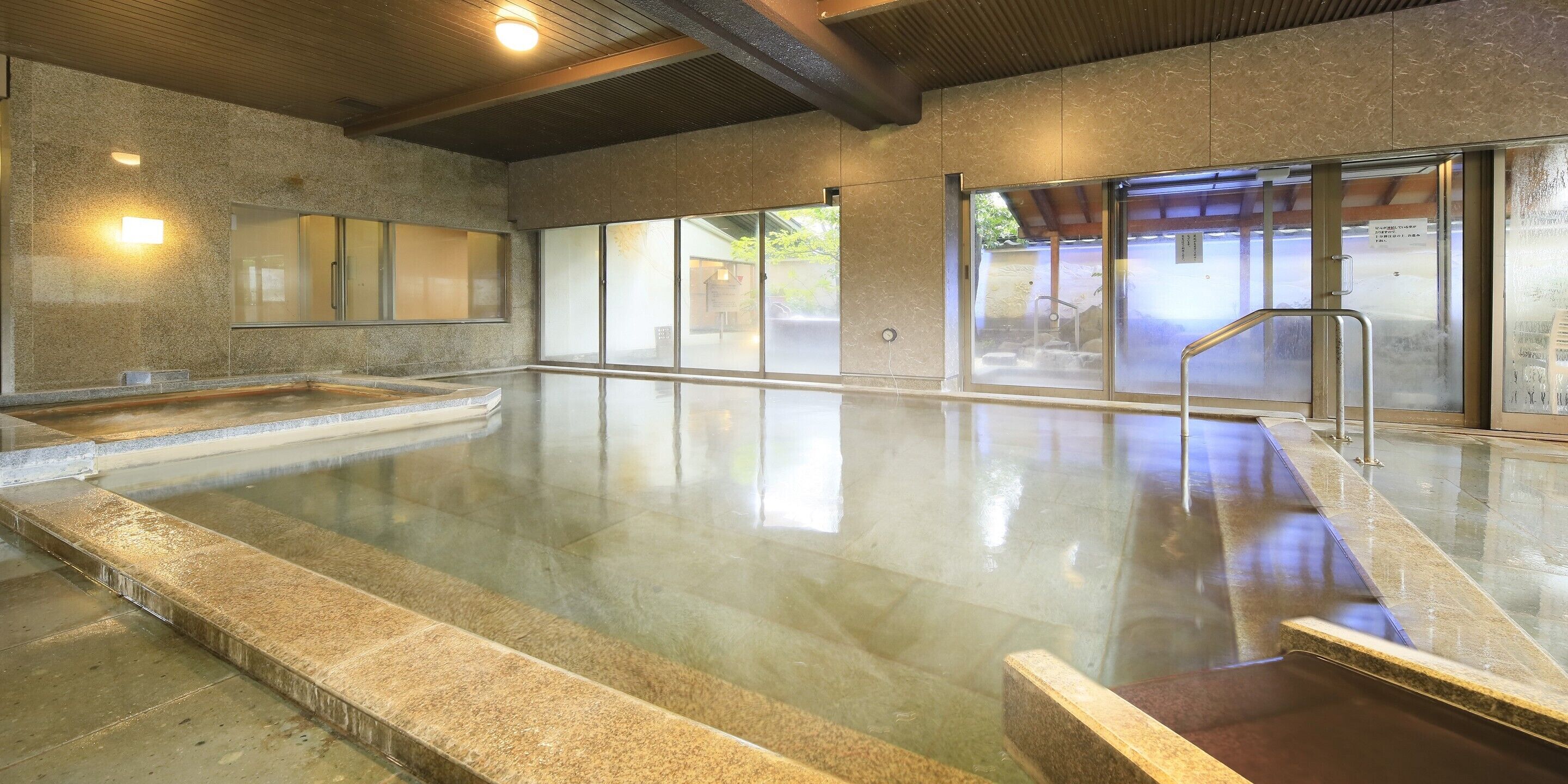 Una amplia piscina interior con paredes de vidrio transparente, suelo de baldosas y techo de madera.