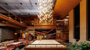 Une auberge japonaise traditionnelle avec des tatamis au sol, un bassin à carpes koï et un luminaire décoratif au plafond.