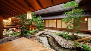 Un intérieur japonais traditionnel avec un sol recouvert de tatamis, un bassin à carpes koï et un pont en bois.