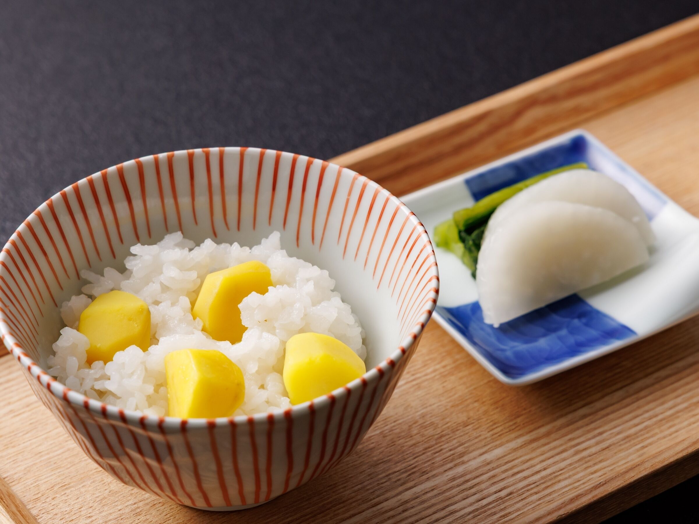 A bowl of white rice with yellow cubes, possibly mango, on a wooden tray.