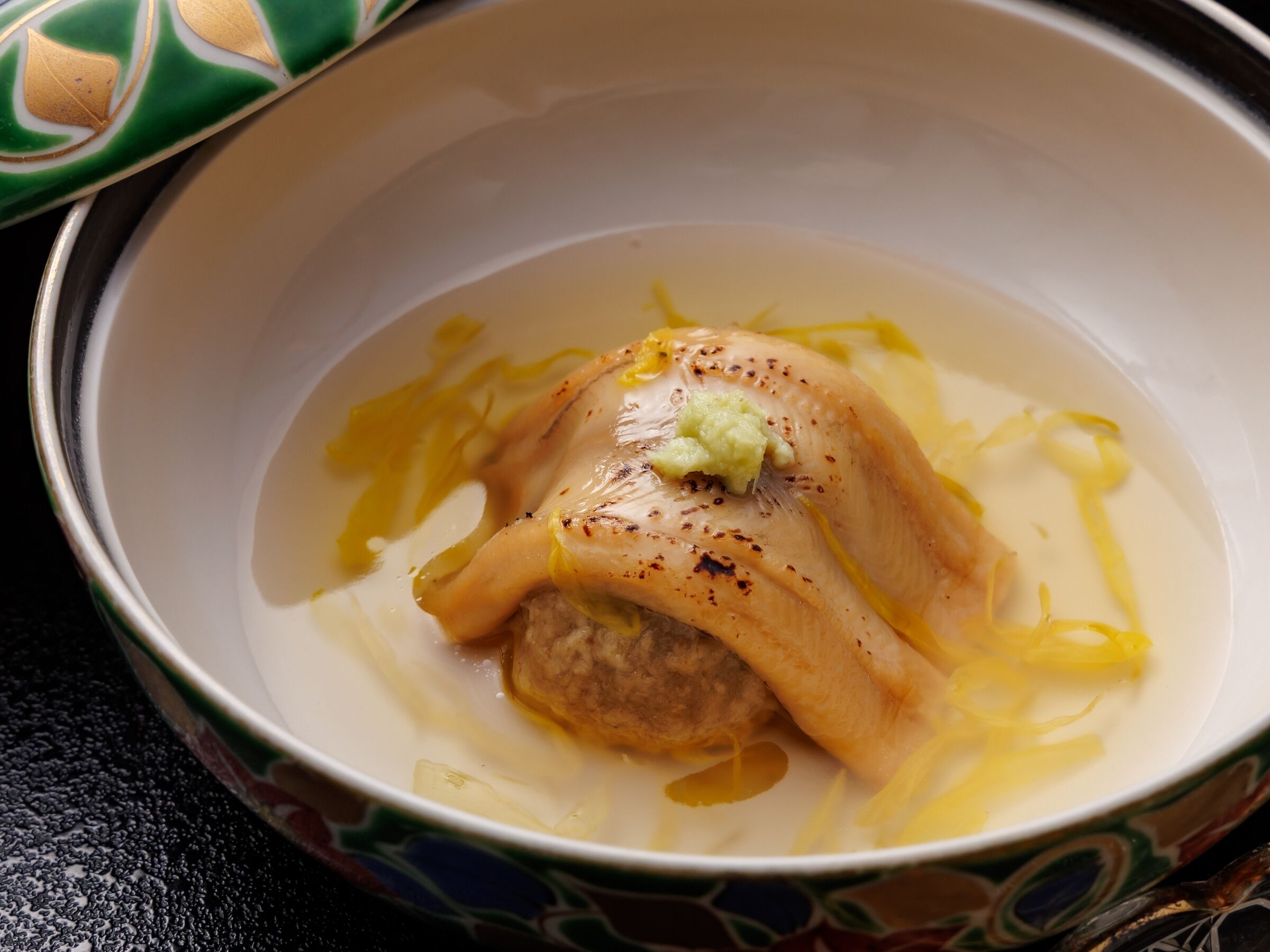 A bowl of soup with a meatball and a dollop of sauce.