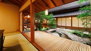 Un intérieur de style japonais traditionnel, avec un sol recouvert de tatamis, des éléments en bois et une vue sur un jardin agrémenté d’un petit étang.