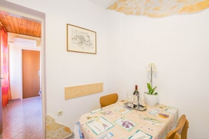 A dining area with a table set for two, a framed artwork on the wall, and a potted plant.