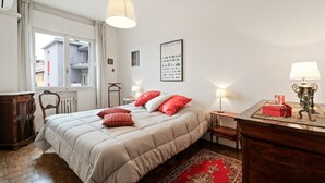 Un dormitorio con una cama, una mesita de noche, una lámpara, un aparador y una ventana.