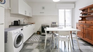 Cocina compacta con lavadora, estufa, mesa de comedor con sillas y un mueble de madera.